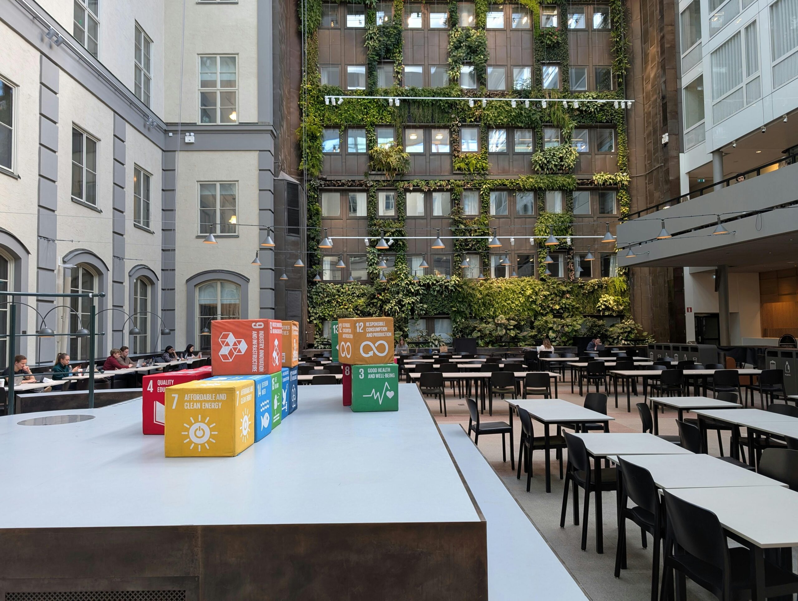 Indoor courtyard with green wall and sustainable development goals displayed on colorful cubes.